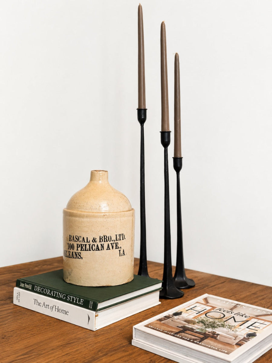 Decorative setup with a ceramic jar, books, and candlesticks on a wooden surface.